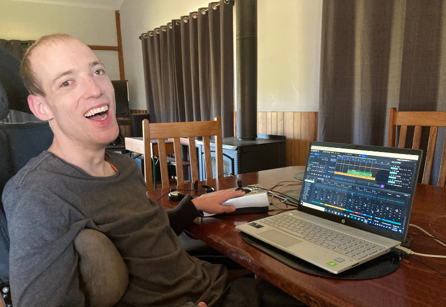 Nathan Johnston, founder of DME3 and Disability Club, using laptop and smiling to camera