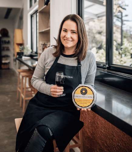 Founder of Barossa Valley Cheese Company Victoria McClurg holding wheel of cheese and glass of wine