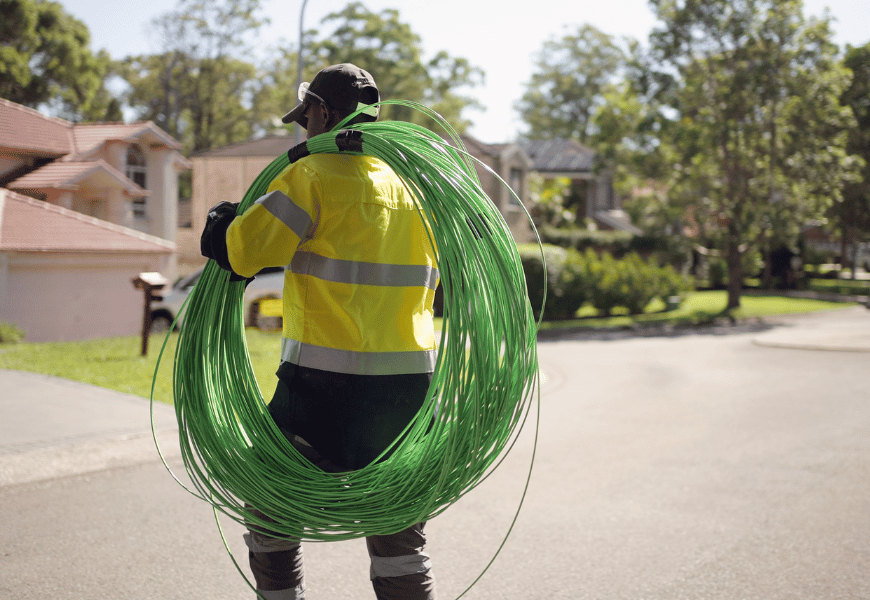 Worker carrying a bundle of green coloured fibre cable as he walks down a street