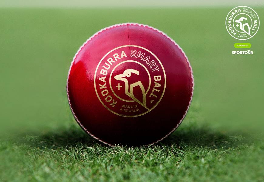 A red Kookaburra Smartball powered by Sportcor sitting on green grass