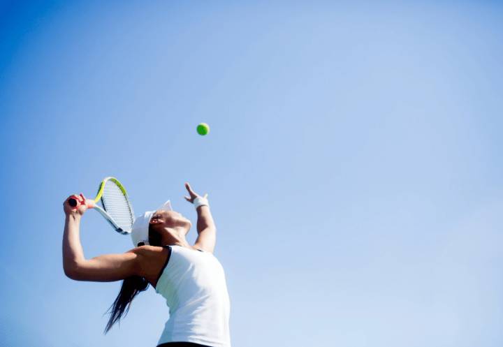 Tennis player serving a tennis ball against a blue sky