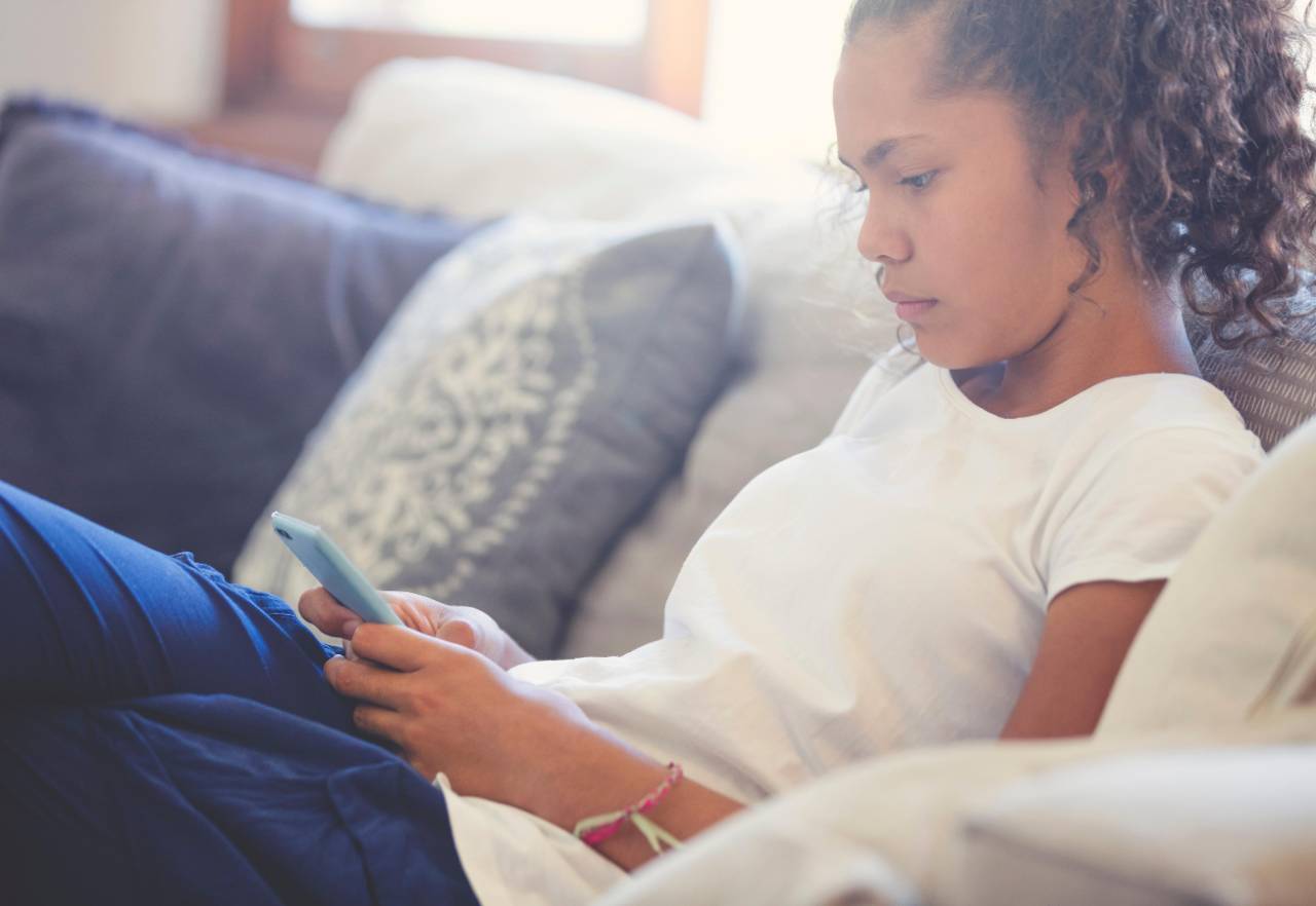 Teenage female sitting on couch looking at mobile phone in her hand