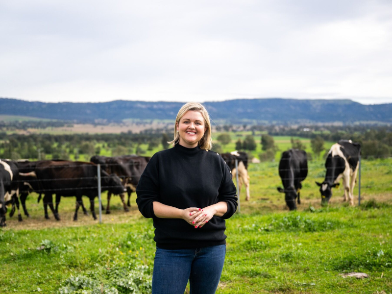 Dimity Smith, Managing Director at GRO Rural, is standing in a lush field with cows grazing nearby