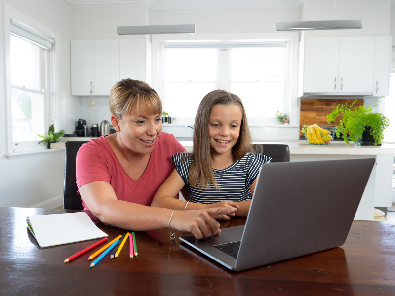 Mother and daughter using a laptop while sitting at their kitchen table
