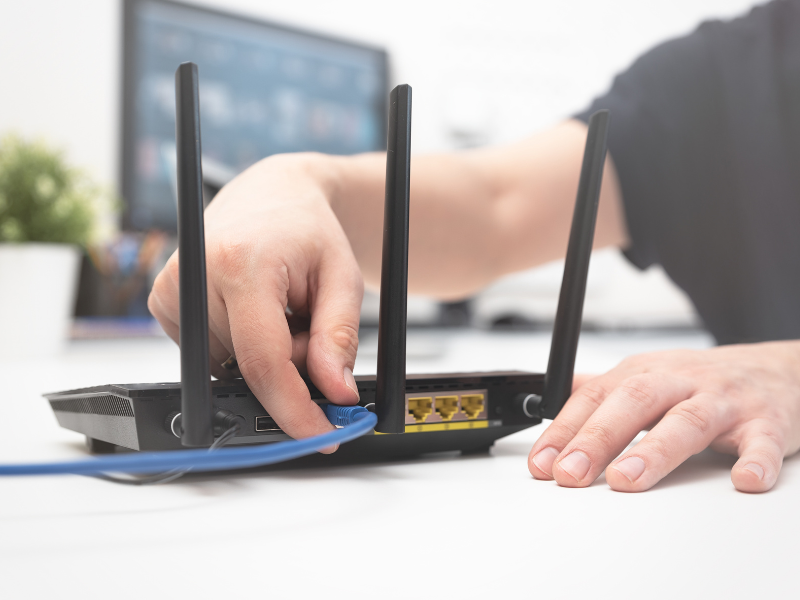 Man plugging in a Wi-Fi router that's sitting on a desk in an office