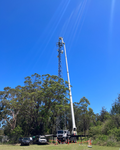 Installing an elevated bird's nest platform on an nbn Fixed Wireless tower with a crane truck against clear sky and leafy trees