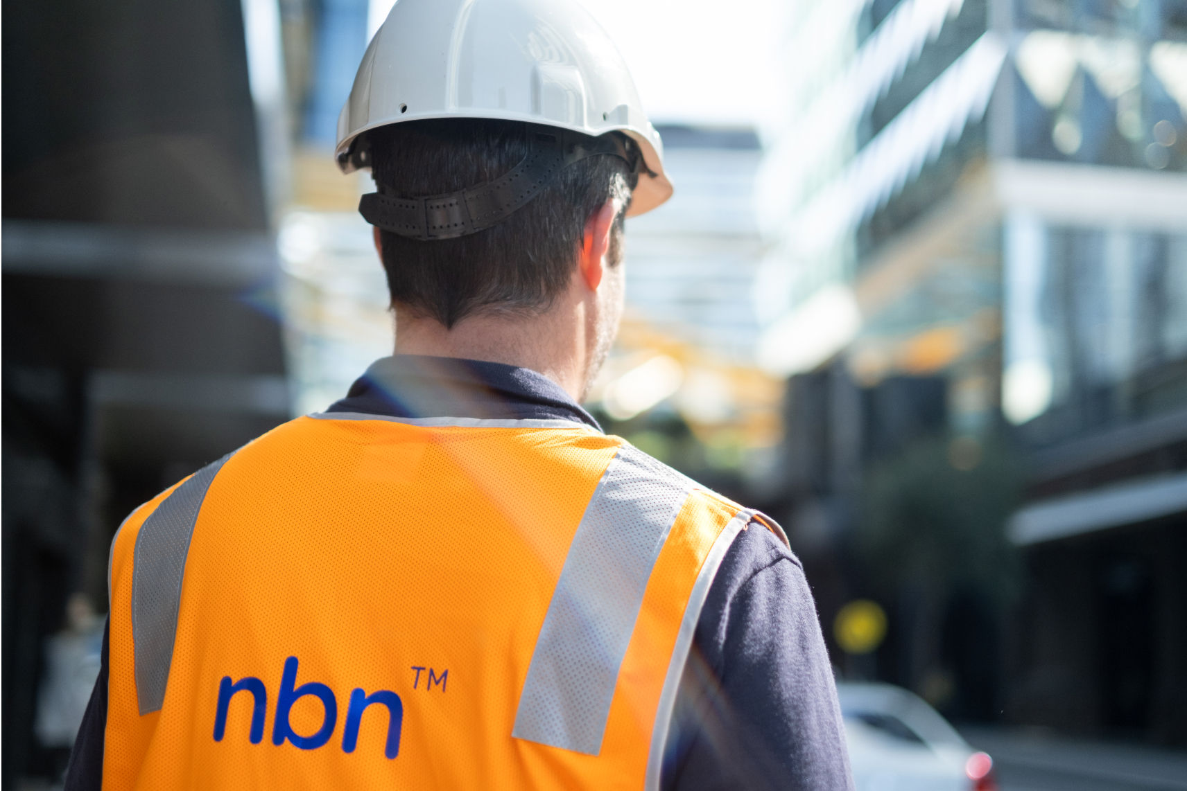 Photo showing an nbn technician wearing a high vis vest and facing a building